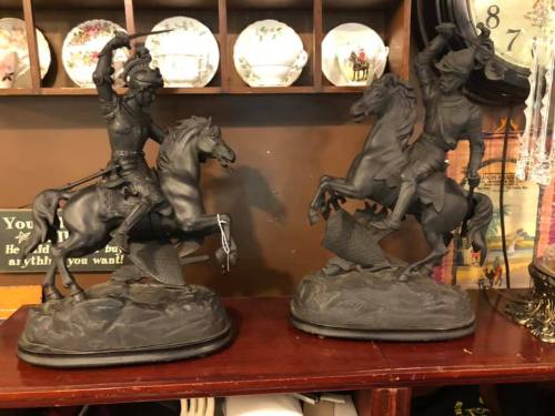 Two black horse statues depicting warriors on horseback, one wielding a sword and the other holding a bow.