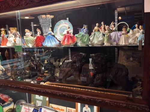 A display case filled with various decorative figurines, including porcelain dolls in colorful dresses and other collectibles.