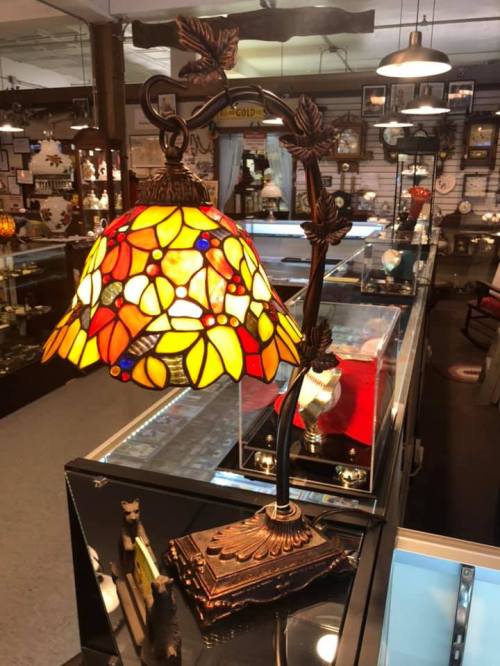 A colorful stained glass lamp with a floral design, displayed in a well-lit shop filled with various decorative items.