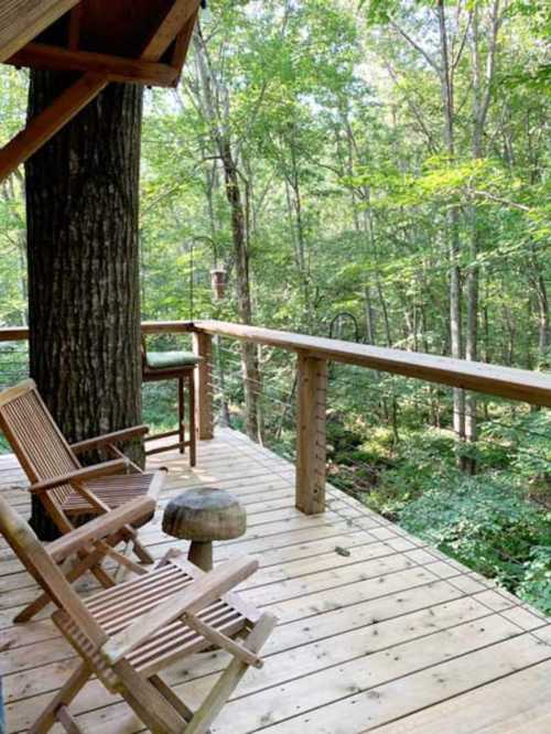 A wooden deck surrounded by trees, featuring two chairs and a small table, creating a serene outdoor space.