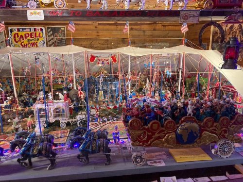 A colorful miniature circus scene with detailed figures, tents, and decorations, illuminated with lights.