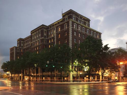 Historic brick building at dusk, illuminated windows, surrounded by trees and streetlights, with a cloudy sky above.