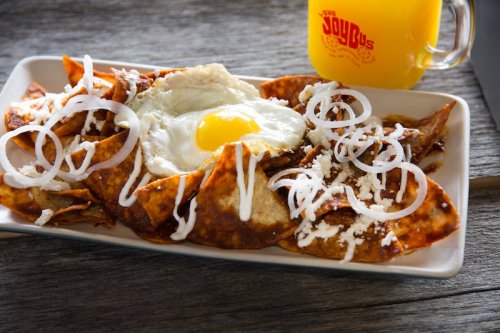 A plate of chilaquiles topped with a fried egg, onions, cheese, and a side of orange juice in a glass.