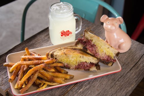 A plate with a sandwich, fries, and a glass of lemonade next to a pink piggy bank on a wooden table.