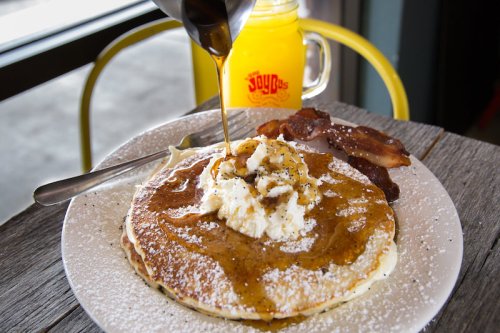 A plate of pancakes topped with syrup and whipped cream, served with bacon and a glass of orange juice.