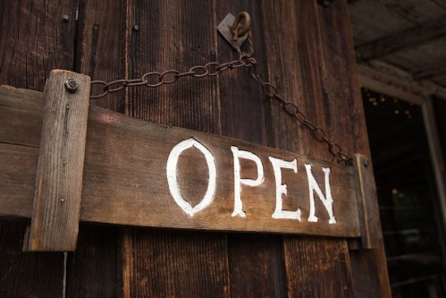 A rustic wooden sign hanging on a door, displaying the word "OPEN" in white letters.
