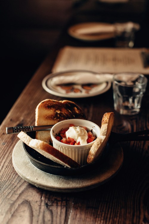 A small bowl of diced tomatoes topped with cream, surrounded by toasted bread slices on a wooden table.