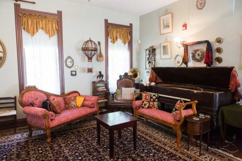 A vintage living room with ornate furniture, a piano, and decorative items, featuring warm colors and a cozy atmosphere.