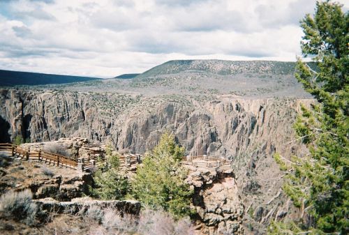 A scenic view of a canyon with rocky cliffs, green trees, and a cloudy sky in the background.