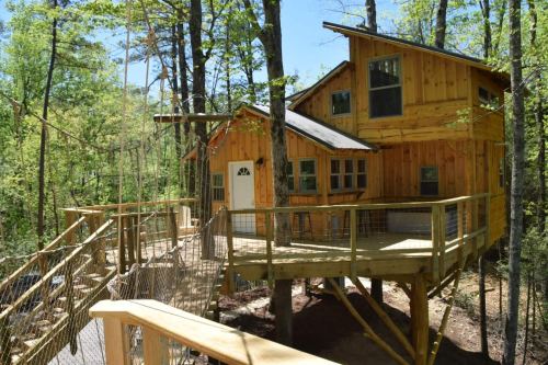 A wooden treehouse surrounded by trees, featuring a deck and rope bridge.