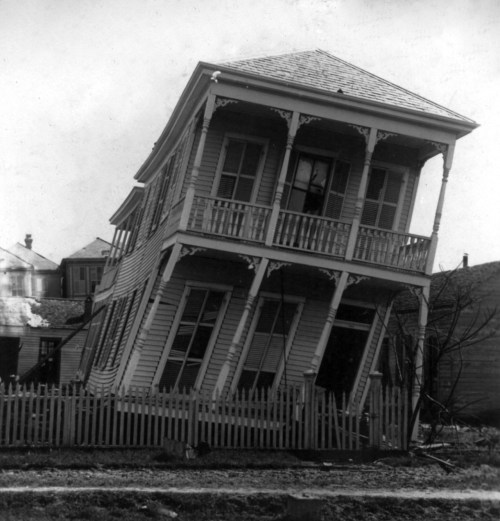 A tilted, historic house with a white picket fence, leaning precariously to one side.