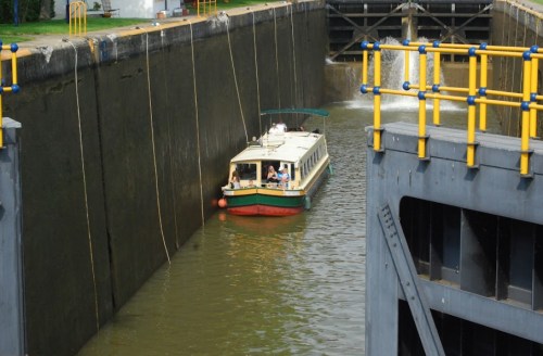 A small boat navigates through a lock chamber, surrounded by concrete walls and yellow railings.