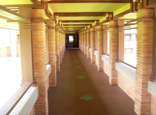 A long corridor with brick columns and a patterned floor, illuminated by natural light.