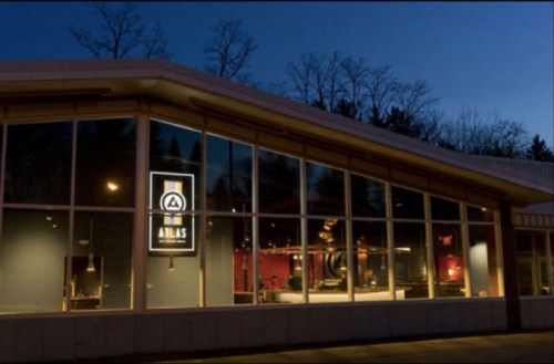 A modern building with large windows, illuminated at dusk, featuring a sign that reads "AIMAS." Trees are visible in the background.