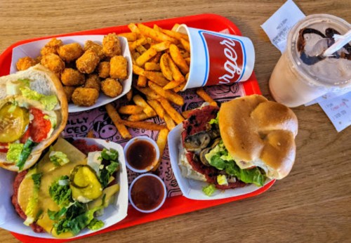 A red tray with two burgers, tater tots, sweet potato fries, and a milkshake.
