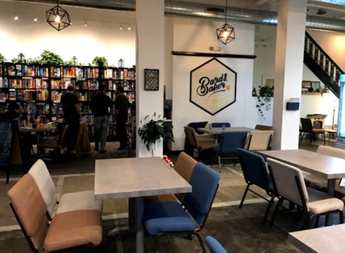 A cozy café with tables and chairs, a bookshelf filled with board games, and people socializing in the background.