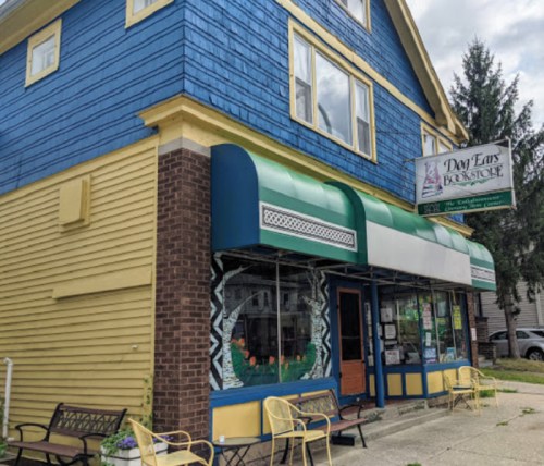 A colorful bookstore with blue and yellow siding, featuring large windows and a sign that reads "Dog Ears Bookstore."