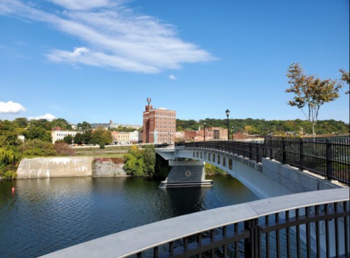 A scenic view of a bridge over a river, with buildings and trees in the background under a clear blue sky.