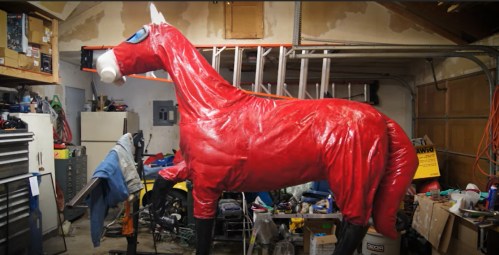 A large, red horse sculpture stands in a cluttered garage filled with tools and various items.
