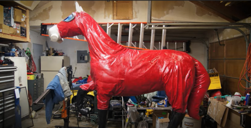 A large, red horse sculpture stands in a cluttered garage filled with tools and various items.