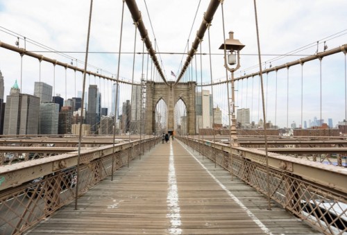 View of the Brooklyn Bridge walkway with city skyline in the background on a cloudy day.