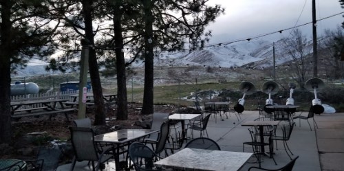 Outdoor seating area with tables and chairs, surrounded by trees and a snowy landscape in the background.