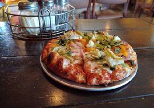 A pizza topped with green peppers, onions, and other vegetables on a metal plate, set on a wooden table.