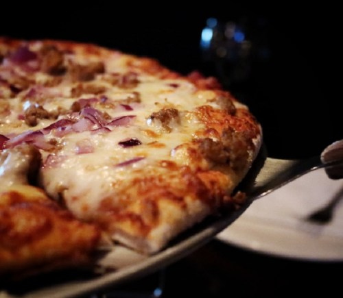 A close-up of a pizza with melted cheese, sausage, and red onion being served on a plate.