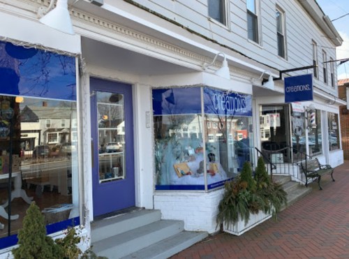 A storefront with blue accents and large windows displaying various items, featuring the sign "Creations."
