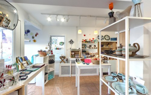 A bright shop interior displaying various handmade crafts, pottery, and decorative items on white shelves.