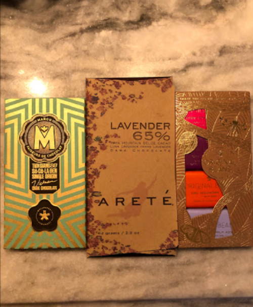 Three chocolate bars displayed on a marble surface, featuring unique packaging designs and flavors.