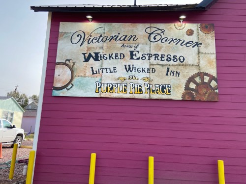 Sign on a pink building reading "Victorian Corner" with "Wicked Espresso," "Little Wicked Inn," and "The Purple Pie Place."