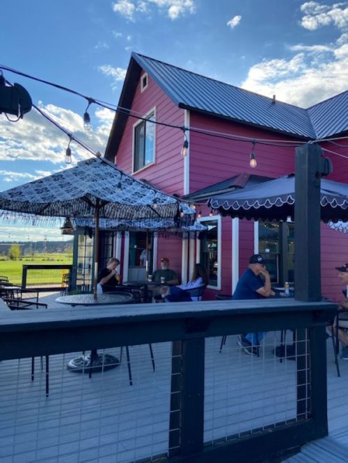 A pink house with a patio, featuring a shaded table and people enjoying the outdoor space under string lights.