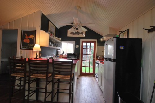 Cozy kitchen with a bar, white cabinets, a black fridge, and a door leading to a garden. Bright and inviting space.