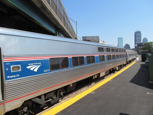 Amtrak sleeping car at a train station, with a city skyline in the background under a clear blue sky.