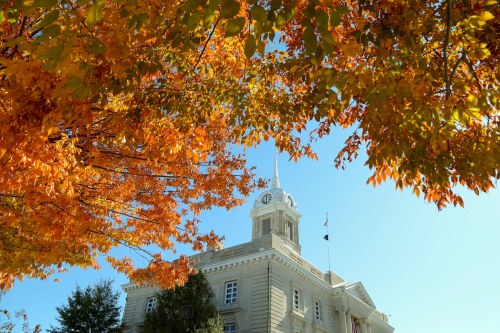 Historic building with a clock tower, framed by vibrant autumn leaves against a clear blue sky.