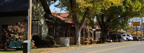 A quaint street scene featuring charming shops, autumn foliage, and parked cars along a tree-lined road.