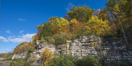 A rocky cliff adorned with vibrant autumn foliage under a clear blue sky.