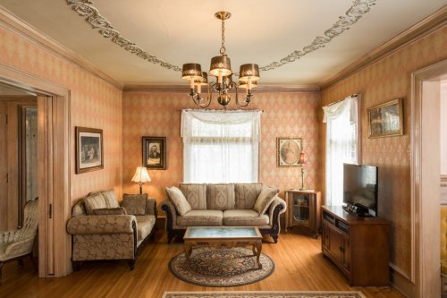 Cozy living room with patterned wallpaper, a chandelier, vintage furniture, and a TV, featuring warm wooden floors.