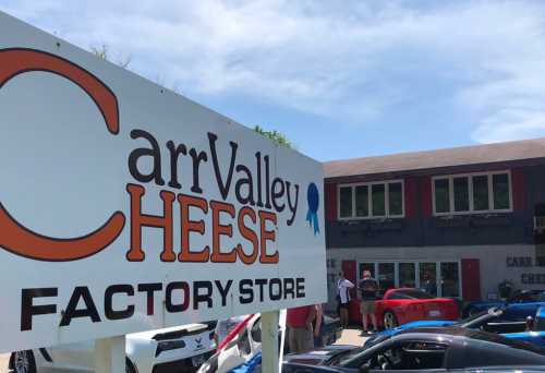 Sign for Carr Valley Cheese Factory Store with cars and people in the background on a sunny day.