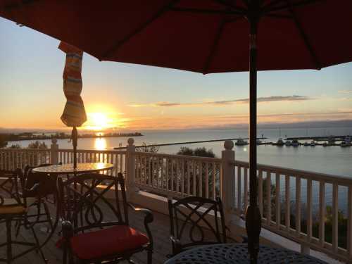 Sunset over a calm bay, viewed from a deck with tables and umbrellas, creating a serene atmosphere.