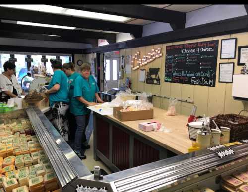 A busy cheese shop with staff in teal shirts preparing orders at a wooden counter, surrounded by various cheese products.