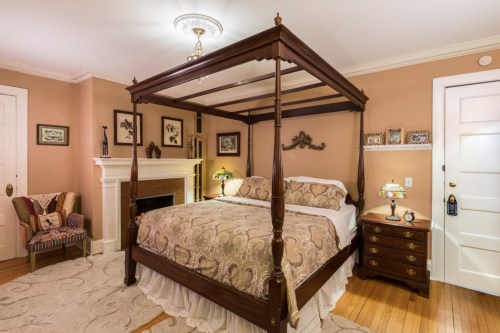 Cozy bedroom featuring a four-poster bed, warm tones, a fireplace, and elegant decor.