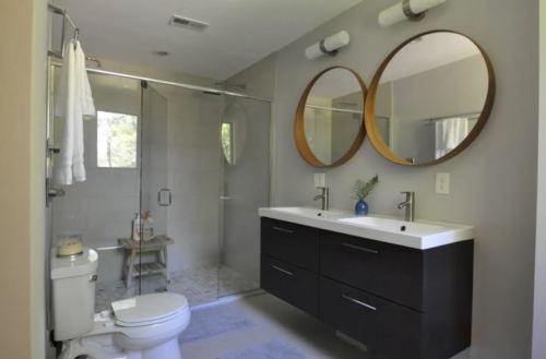 Modern bathroom featuring a double vanity, round mirrors, a glass shower, and neutral tones.