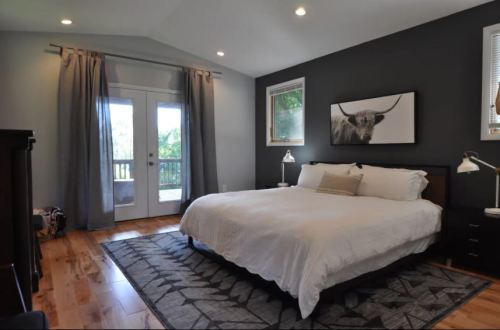 A modern bedroom with a large bed, gray walls, and a cow print artwork, featuring natural light from double doors.