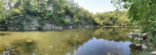 A serene lake surrounded by lush greenery and rocky cliffs under a clear blue sky.