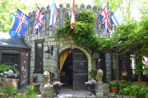 A whimsical stone castle entrance adorned with flags, surrounded by greenery and colorful flowers.