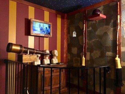 A room with striped walls, a telescope, sculptures, and a TV, featuring a rustic wooden cabinet and decorative elements.