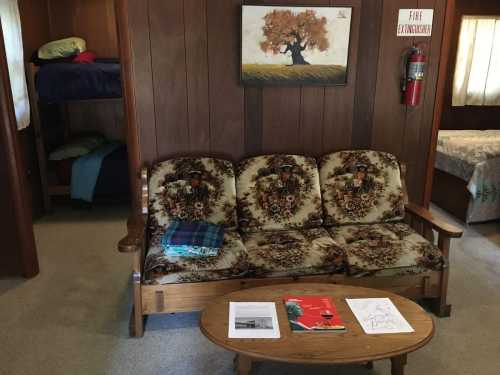 Cozy interior with a floral couch, wooden table, and bunk beds in the background, featuring warm wood paneling.