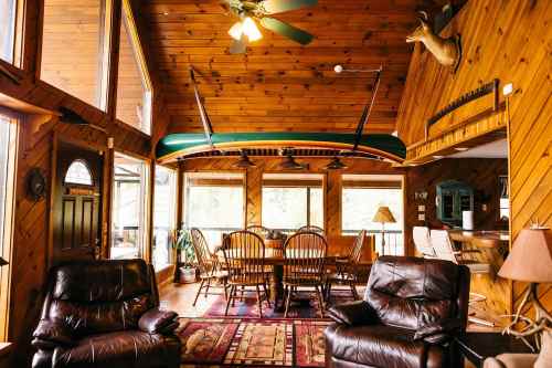 Cozy wooden interior with a dining area, leather chairs, and a canoe mounted on the wall, featuring large windows.